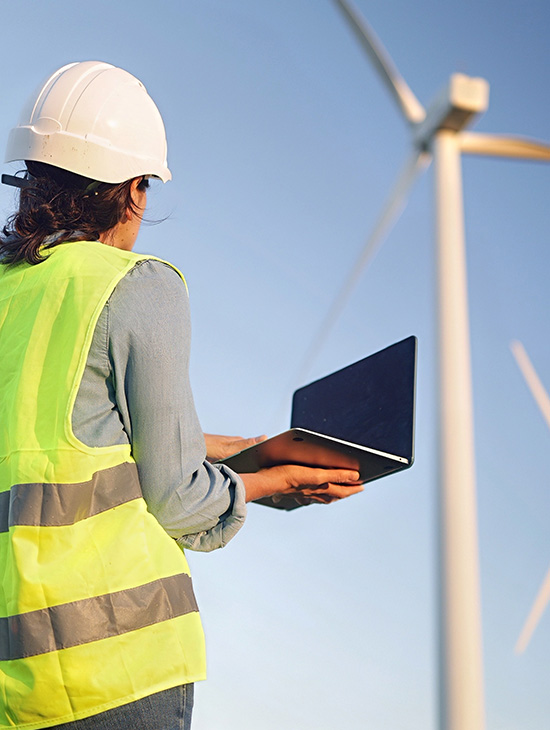 worker in safety gear operating laptop near wind turbines in renewable energy sector analyzing performance data for sustainable solutions