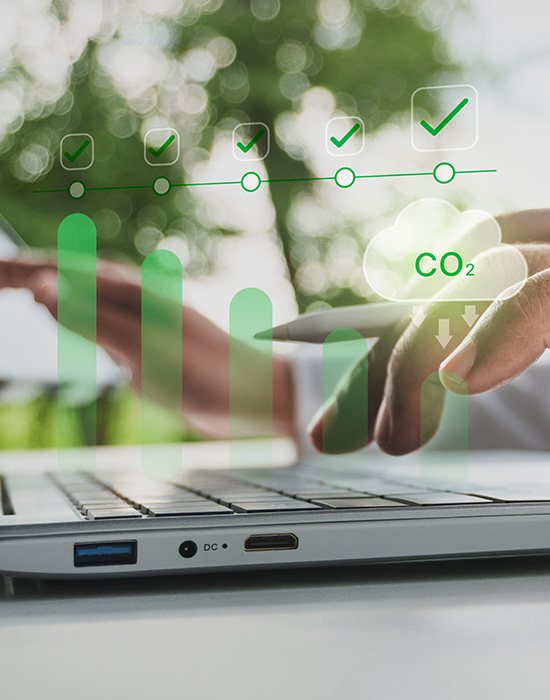 hands typing on a laptop with green upward trend bar graph and CO2 cloud indicators representing sustainability and environmental progress in 21st century technology