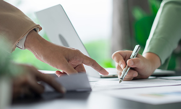 hands pointing to documents while one person writes notes on a desk with a laptop in the background five important aspects of collaboration