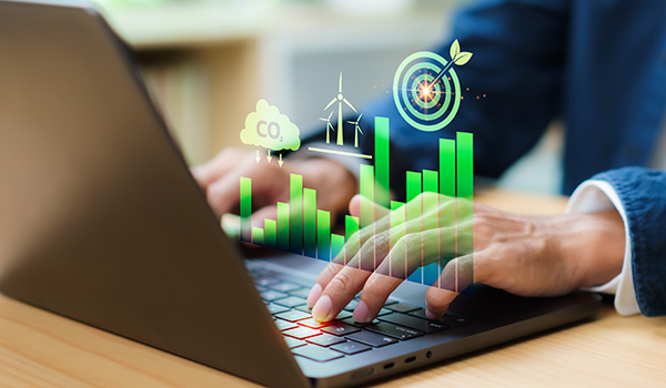person typing on laptop with digital graphs and eco icons representing sustainability and carbon reduction