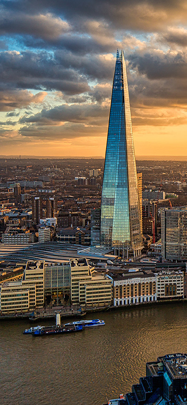 The Shard skyscraper rising above London skyline at sunset with clouds and the River Thames in foreground highlighting urban architecture and city life at 18 stories tall